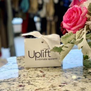Image of Uplift Intimate Apparel gift card on granite countertop near a floral display.